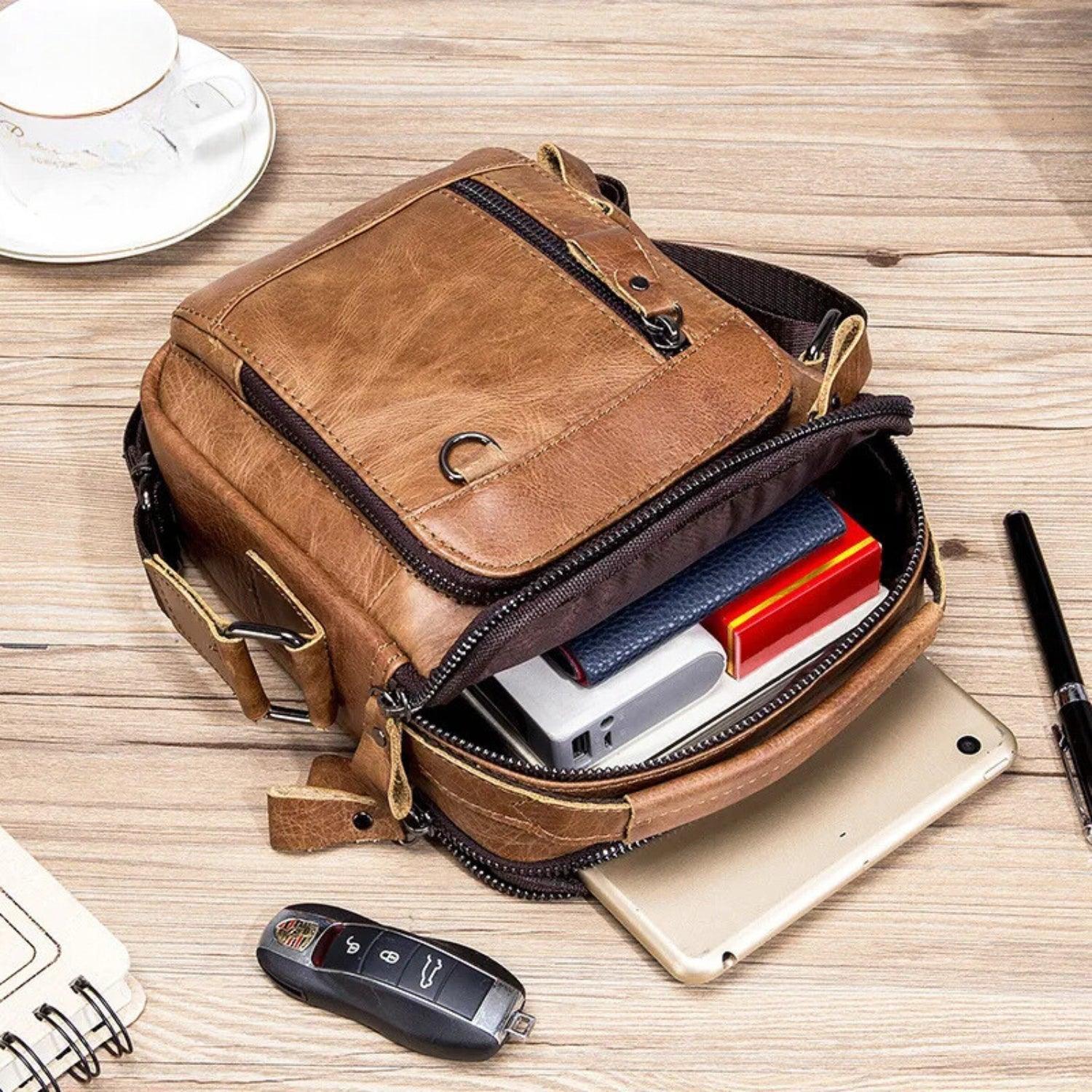 Bolso compacto de piel para hombre, interior organizado con accesorios sobre mesa de madera