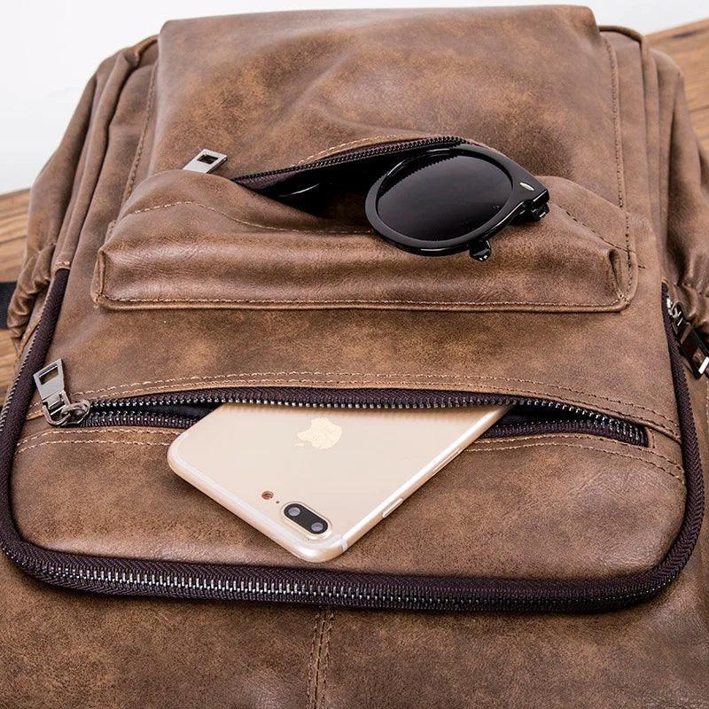 Mochila masculina de cuero compacta color marrón con gafas y celular en bolsillos